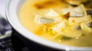 Un tazón de sopa con ingredientes visibles como tofu y posiblemente verduras en un caldo transparente.
