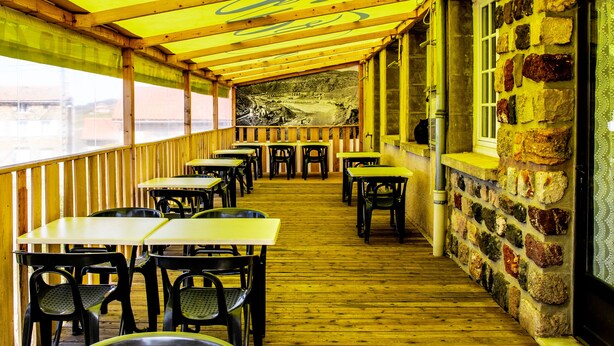 Un espacio de comedor al aire libre cubierto con mesas y sillas, paredes de piedra y vigas de madera.