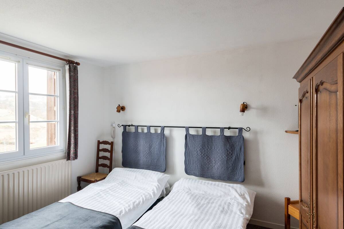 A bedroom with two beds, a wooden wardrobe, a window with curtains, and a radiator.