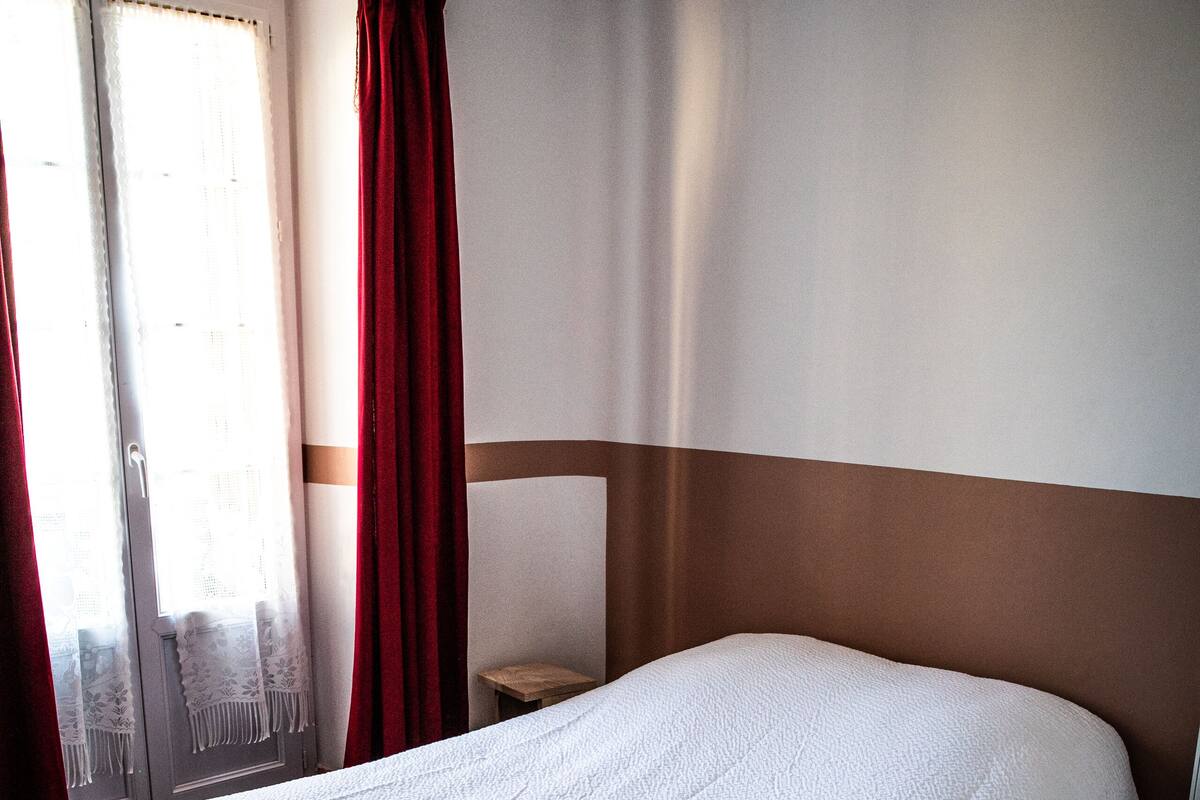 A hotel room with a large bed, a bedside table, and a window with curtains.