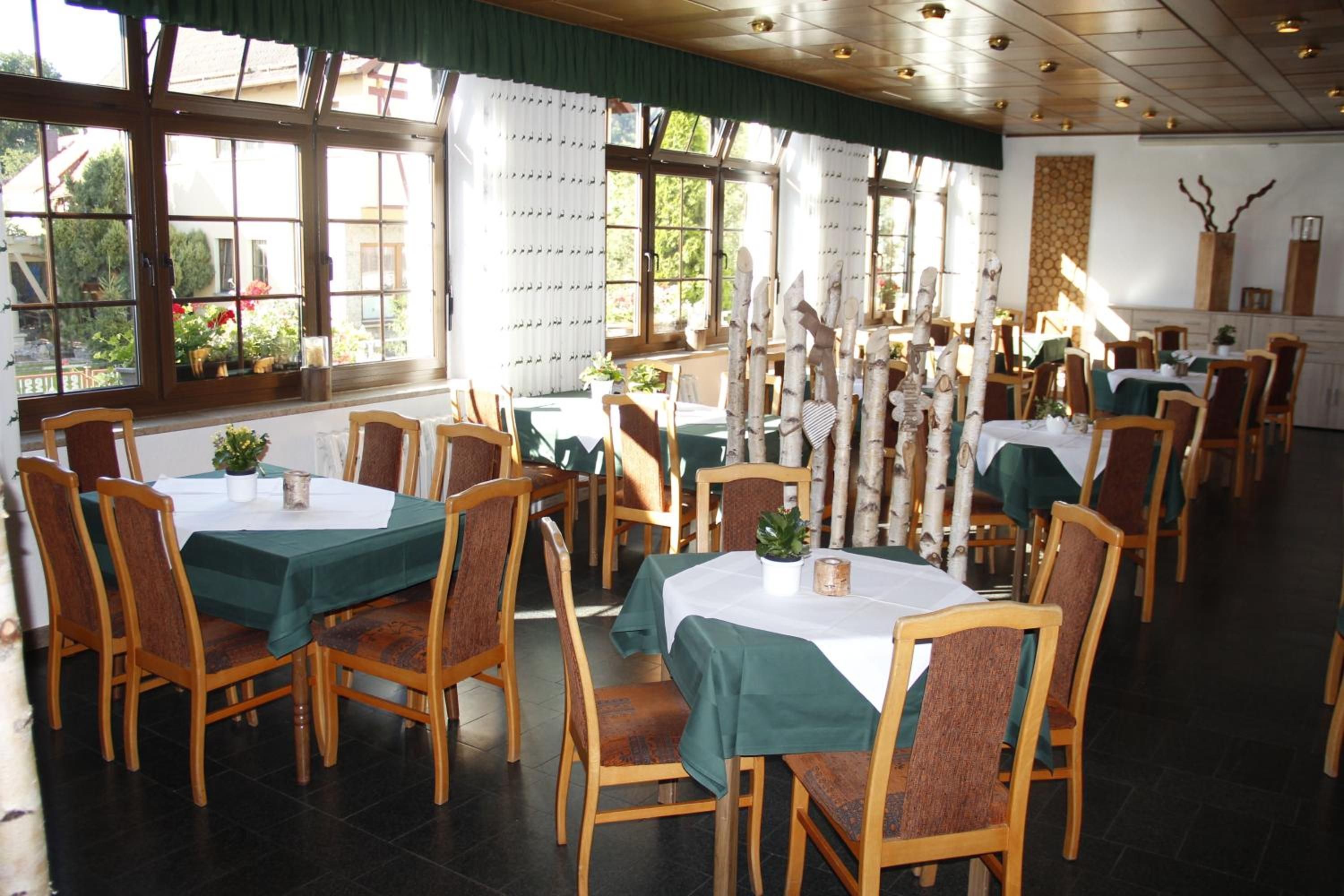 A dining area with multiple tables and chairs, large windows with curtains, and a tiled floor.