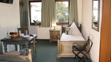 A compact hotel room with a bed, a small table with a lamp, a chair, and a view of the outdoors through the window.