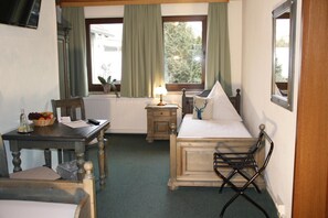 Habitación de hotel pequeña con una cama, una mesita con lámpara, una silla y vistas al exterior a través de la ventana.