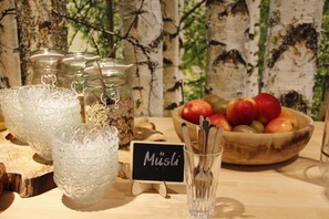 A table with glass jars, a bowl of apples, and a sign reading 'Müslü'.