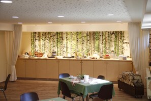 A dining area with a long table, chairs, and a wall with a nature-themed wallpaper.