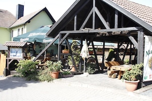 Una estructura de madera tradicional con techo a dos aguas, una rueda y asientos al aire libre.