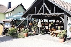 A traditional wooden structure with a pitched roof, a wheel, and outdoor seating.