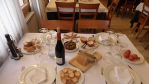 Una mesa de comedor dispuesta con platos, pan, aceitunas, queso y copas de vino.