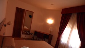 Una habitación de hotel con una cama, un escritorio, una silla, una lámpara y una ventana con cortinas.