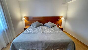 Una cama individual con cabecera de madera, dos mesitas de noche y una colcha estampada.