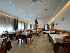 Een restaurant met meerdere tafels en stoelen, een betegelde vloer en een plafond met inbouwverlichting.