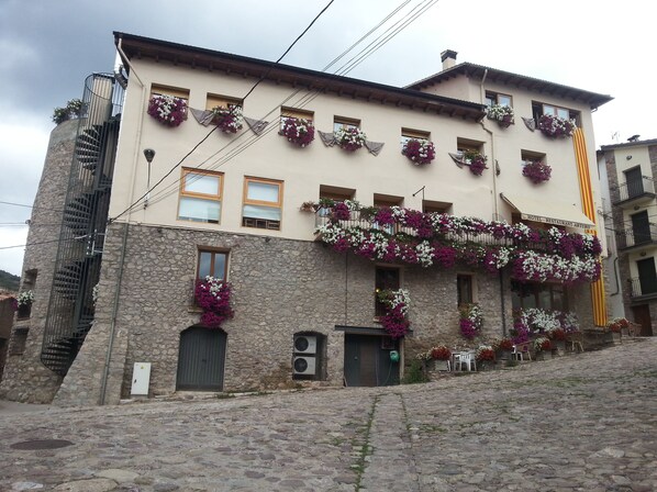 Ein Gebäude mit mehreren Balkonen, die mit Blumen geschmückt sind, einer Steinfassade und einem Schild, das es als Hotel und Restaurant kennzeichnet.