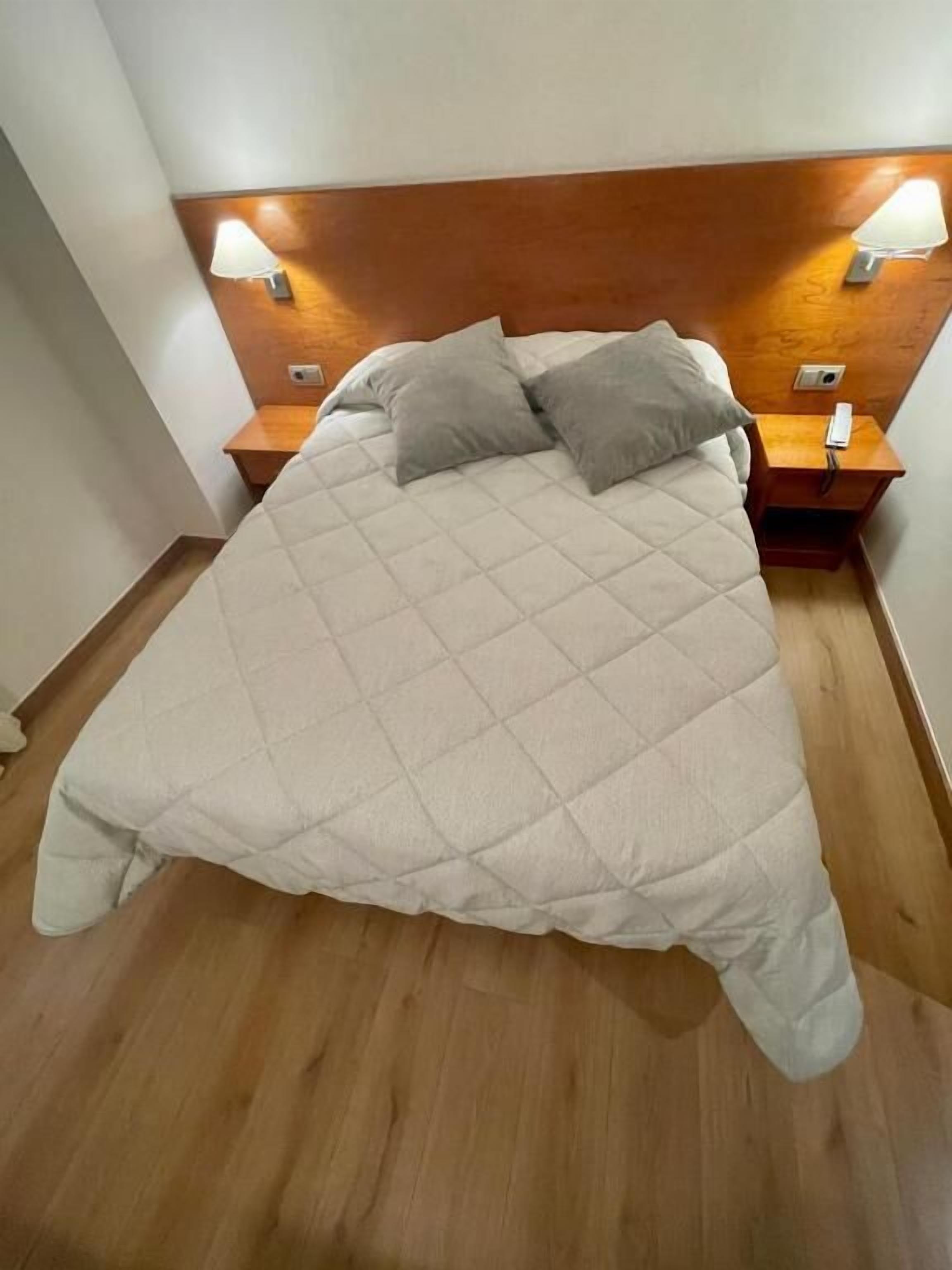A bed with a quilted cover, two bedside lamps, and a wooden headboard.