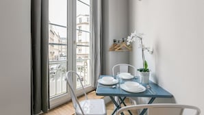Comedor con una mesa dispuesta para dos, una orquídea en maceta y vistas de edificios a través de una ventana.