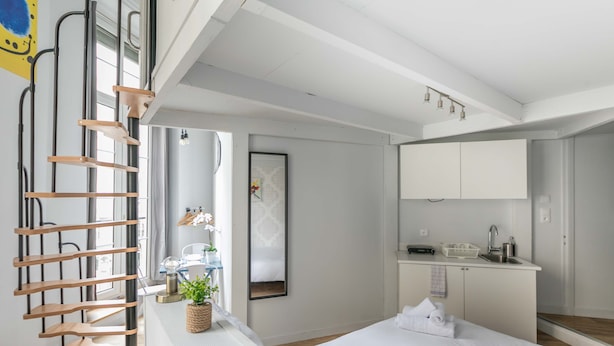 Una habitación de hotel moderna con una escalera de madera, una cama, una pequeña cocina y un ventanal grande.