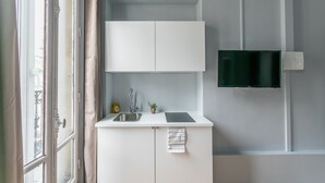 Una cocina compacta con un lavamanos integrado, una pequeña encimera y un televisor de pantalla plana montado en la pared.