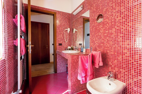 Ein Badezimmer mit roten Fliesenwänden, einer Holztür, einem Waschbecken, einem Spiegel und einem Handtuchhalter.