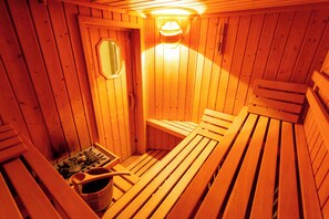 A sauna with wooden benches and a bucket of rocks. - Hotel Alesi (Malcesine)