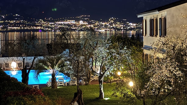 Vista noturna de uma propriedade à beira-mar com piscina, árvores e um edifício com colunas.