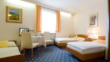 Een hotelkamer met twee enkele bedden, een bureau met stoel, een klein tafeltje en een raam met gordijnen.