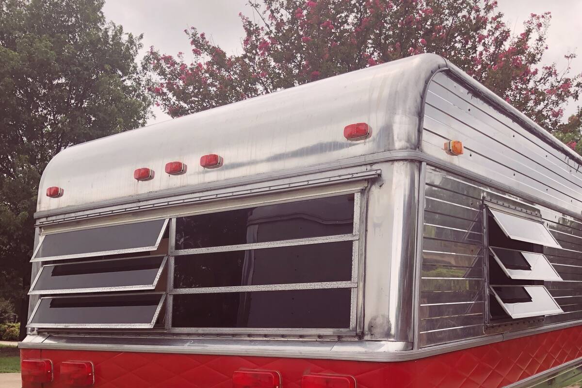 A vintage bus with a red and silver exterior, featuring a rear window, a license plate, and a red bumper.