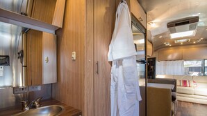 Ein kompaktes Wohnmobil-Interieur mit einem Holzkasten, einem Waschbecken, einem aufgehängten Handtuch und einer Couch im Wohnbereich.