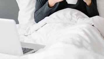 A person sitting on a bed with a laptop and holding a mug.