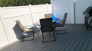 En udendørs terrasse med et bord, stole, grill og et hvidt gelænder.