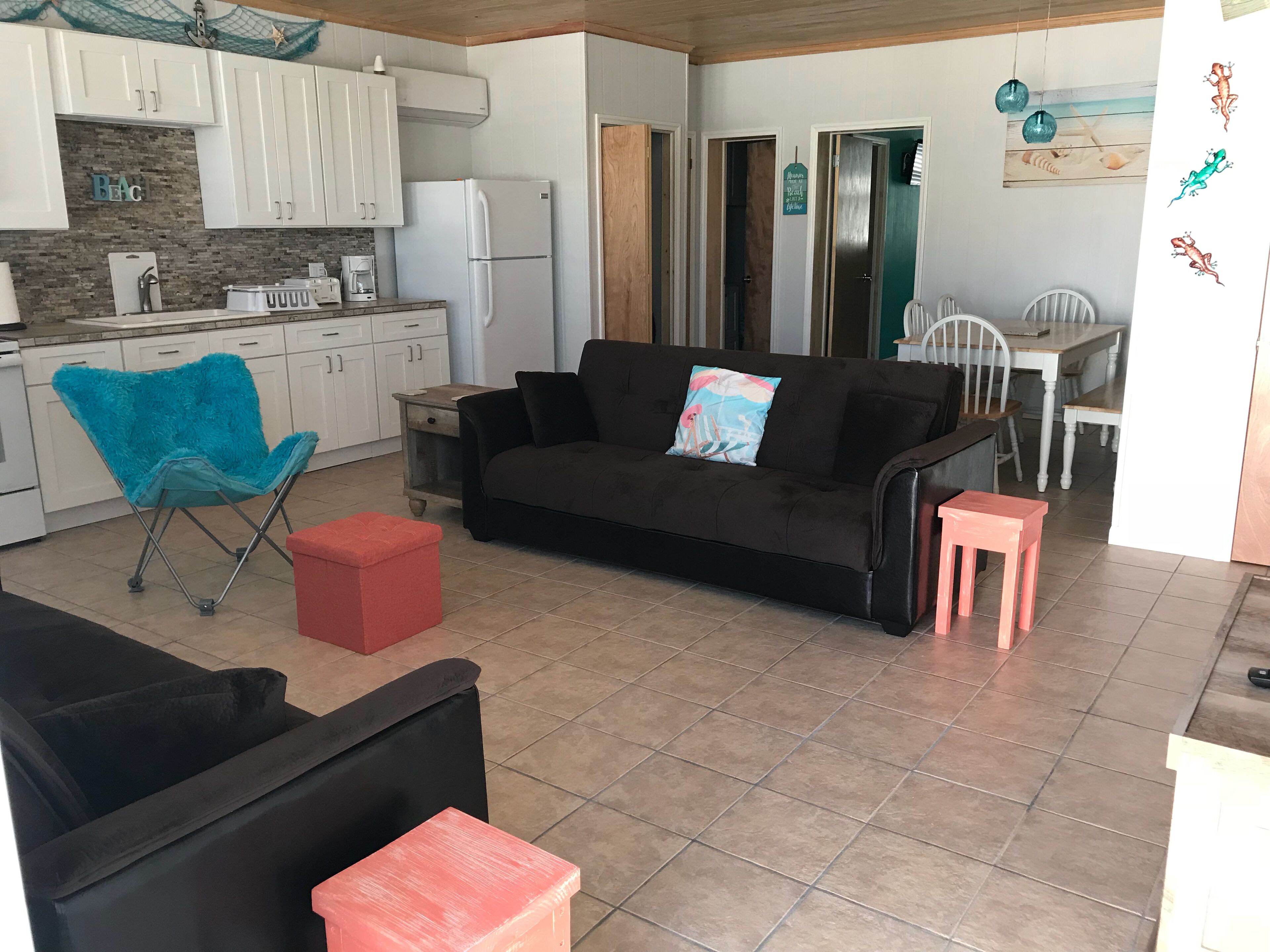 Una sala de estar con un sofá, una mesa de centro y una silla. Hay una zona de cocina con armarios y electrodomésticos.