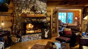 A cozy log cabin interior with a stone fireplace, wooden furniture, and a television mounted on the wall. - Fully furnished log home in one of northern Wisconsin's last wilderness areas (Mercer)