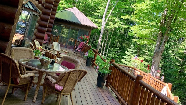 A wooden deck with wicker furniture, a glass table, and a view of a forested area. - Fully furnished log home in one of northern Wisconsin's last wilderness areas (Mercer)