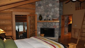 A cozy log cabin bedroom with a stone fireplace, wooden beams, and a view of the outdoors. - Fully furnished log home in one of northern Wisconsin's last wilderness areas (Mercer)