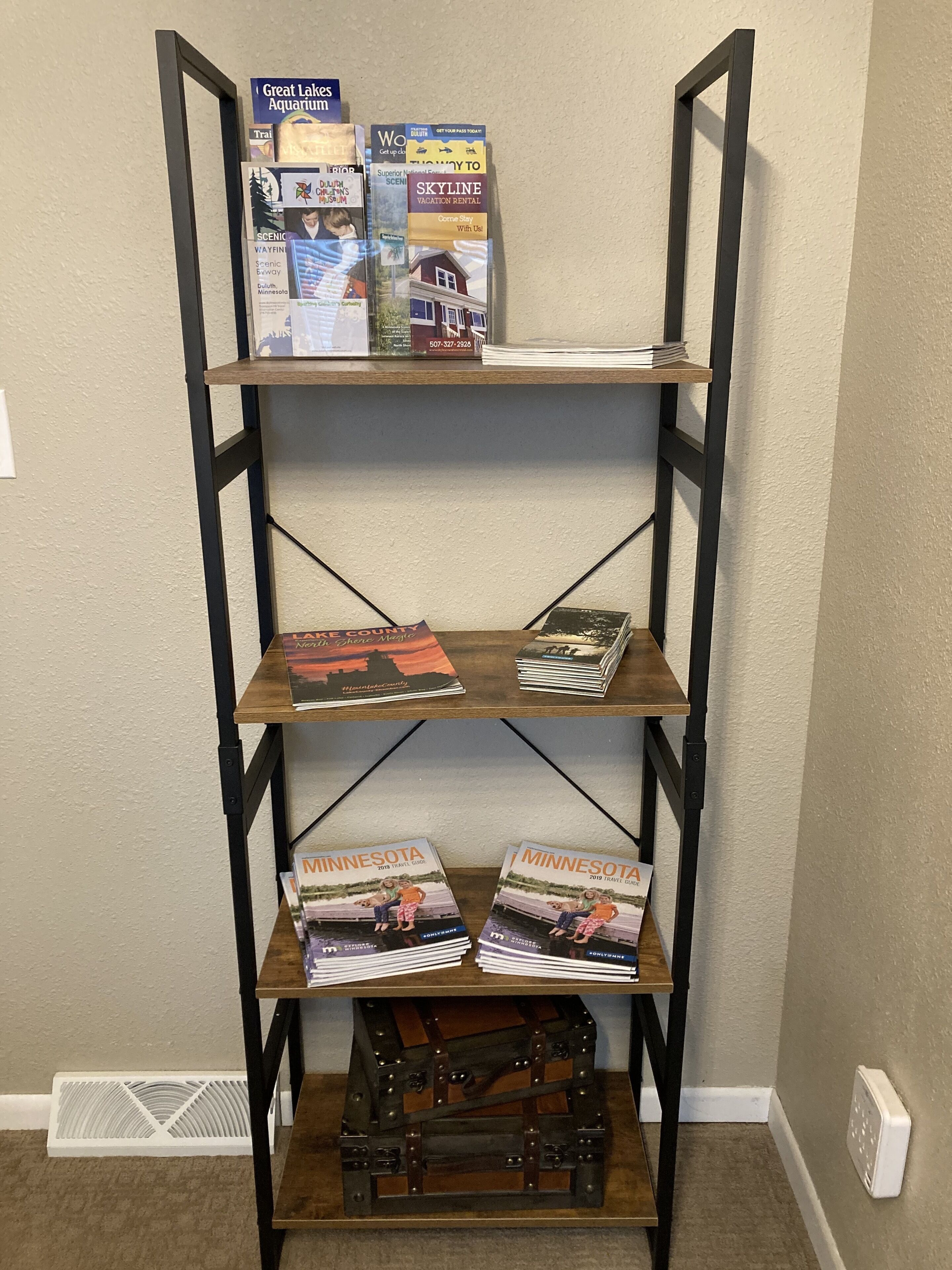 A metal shelving unit with travel brochures and a small chest at the bottom.
