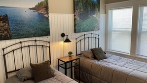 Een slaapkamer met twee bedden, een nachtkastje, een lamp en twee grote landschapsschilderijen aan de muur.