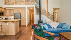 Un vaste espace de vie aménagé dans un style industriel, avec une cuisine, un canapé bleu et un escalier en bois.
