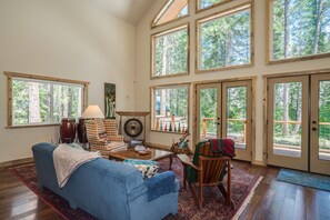 Ein geräumiges Wohnzimmer mit einem blauen Sofa, einem Holztisch und einem großen Fenster mit Blick auf einen Wald.
