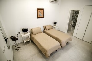 A bedroom with two single beds, a bedside table with a lamp, a framed picture on the wall, and a door leading to another room. - Probably the best view In Malta (L-Isla)