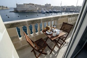 A balcony with a table set for breakfast, overlooking a marina with boats and a historic building in the background. - Probably the best view In Malta (L-Isla)