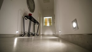 A hallway with a polished floor, a wall-mounted mirror, a small table with a red object, and a window with blinds. - Probably the best view In Malta (L-Isla)