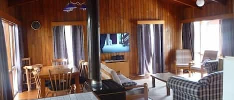 A wooden interior with a dining area, sofa, TV, and a fireplace.