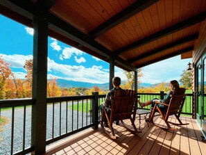 A covered deck with wooden flooring and metal railings, overlooking a scenic view of autumn foliage and distant mountains. - Romantic Mountain Log Cabin #3 Escape with Hot Tub & mountain views Near Luray (Luray)