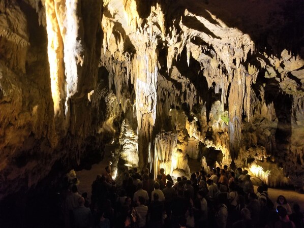 A cave with stalactites and stalagmites, illuminated by artificial lighting, with visitors exploring the formations. - Romantic Mountain Log Cabin #3 Escape with Hot Tub & mountain views Near Luray (Luray)