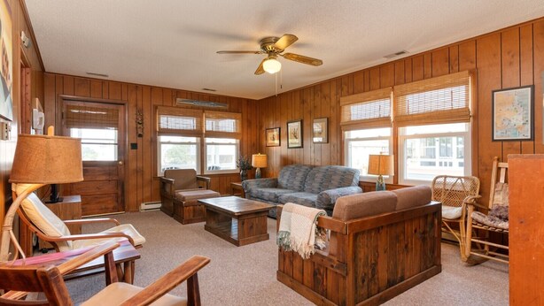 A cozy living room with wooden walls, a ceiling fan, and a large window with blinds. - 401 Dog-Friendly - minutes to Beach Access & YMCA (Nags Head)