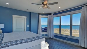 A bedroom with a large bed, a ceiling fan, and a view of the beach. - Stunning Ocean View Retreat w/ Spacious Balcony & Pool Access (Tybee Island)