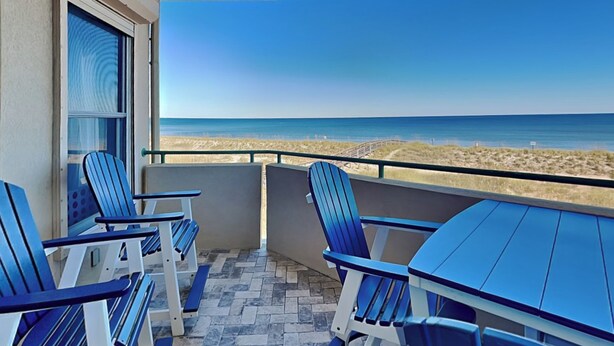 A balcony with a view of the beach, featuring blue chairs and a table. - Stunning Ocean View Retreat w/ Spacious Balcony & Pool Access (Tybee Island)