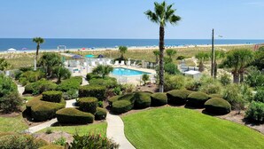 A landscaped area with a swimming pool, palm trees, and a view of the beach. - Stunning Ocean View Retreat w/ Spacious Balcony & Pool Access (Tybee Island)