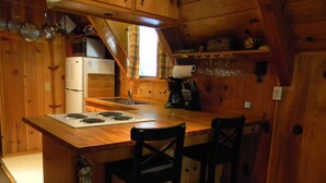 Cucina di una baita in legno con isola centrale, sgabelli da bar, frigorifero e macchina del caffè.