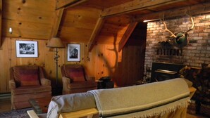 Un accogliente interno di una baita di legno con una panca, due poltrone, un camino e un muro in mattoni.