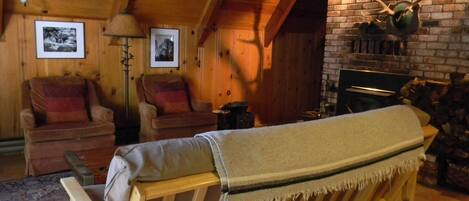 Un acogedor interior de cabaña de madera con un banco, dos sillones, una chimenea y una pared de ladrillo.