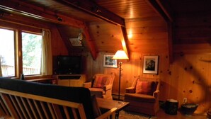 Un interno accogliente con una panca di legno, due poltrone, un televisore e una lampada da terra.